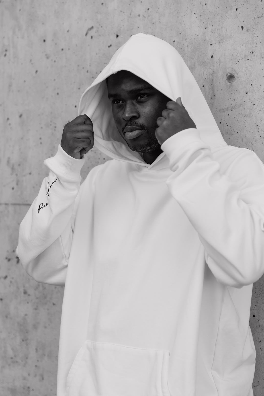 Man wearing white hoodie in front of concrete wall